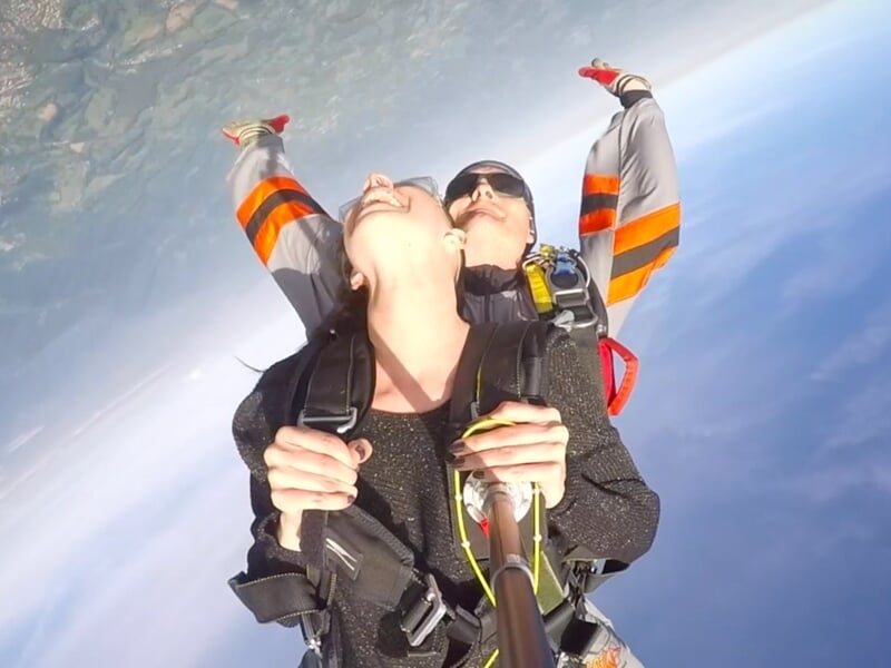 Saut en parachute tandem, deux personnes en chute libre avec ciel bleu et nuages.