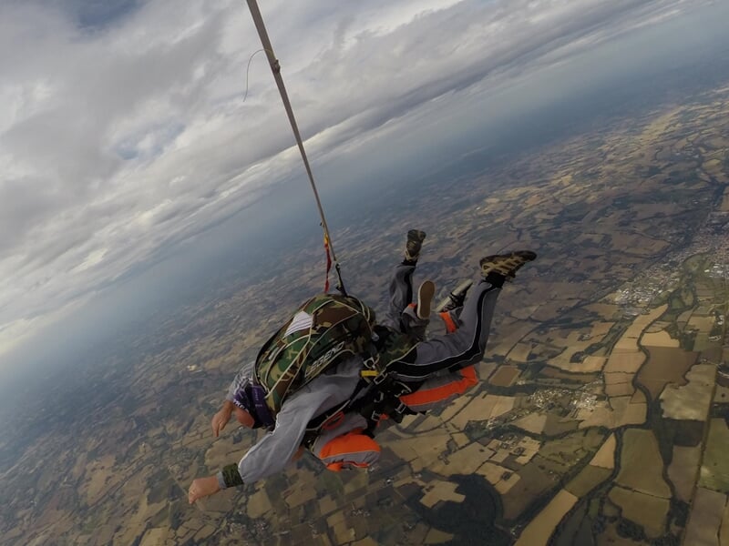 Parachutiste en chute libre, bras écartés avec ciel bleu et nuages blancs.