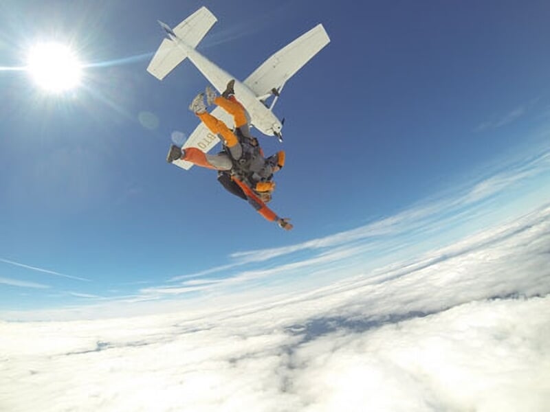 Personne en parachute en chute libre, vue rapprochée avec ciel bleu et nuages.