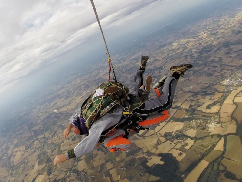 Deux personnes en chute libre lors d'un saut en parachute au-dessus des champs et villages de Villefranche-de-Rouergue.