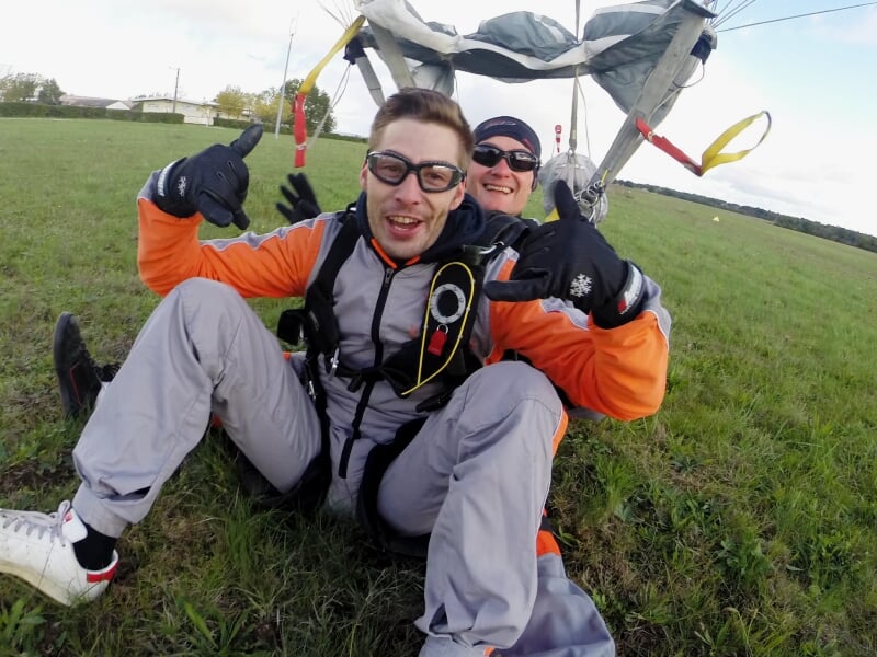 Parachutistes en tandem en chute libre au-dessus d'un aéroport avec ciel bleu.