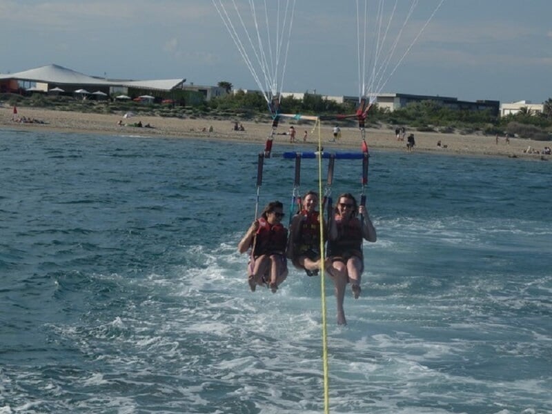 Trois personnes en parachute ascensionnel rouge, blanc et bleu, suspendues au-dessus de la mer.