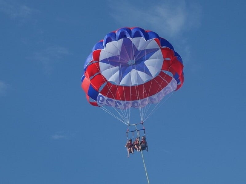 Trois personnes en parachute ascensionnel coloré rouge, blanc et bleu, flottant dans le ciel clair.