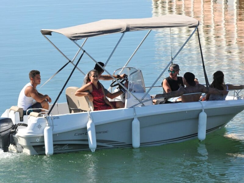 Groupe de personnes assises dans un bateau blanc avec toit, naviguant sur une eau calme au port.