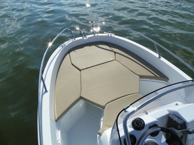 Avant d'un bateau blanc avec coussins beiges, volant et tableau de bord visible, sur une eau calme.