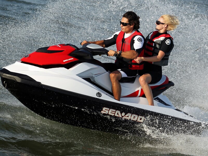 Deux personnes en gilets rouges pilotent un jetski blanc et rouge sur une mer agitée avec éclaboussures.