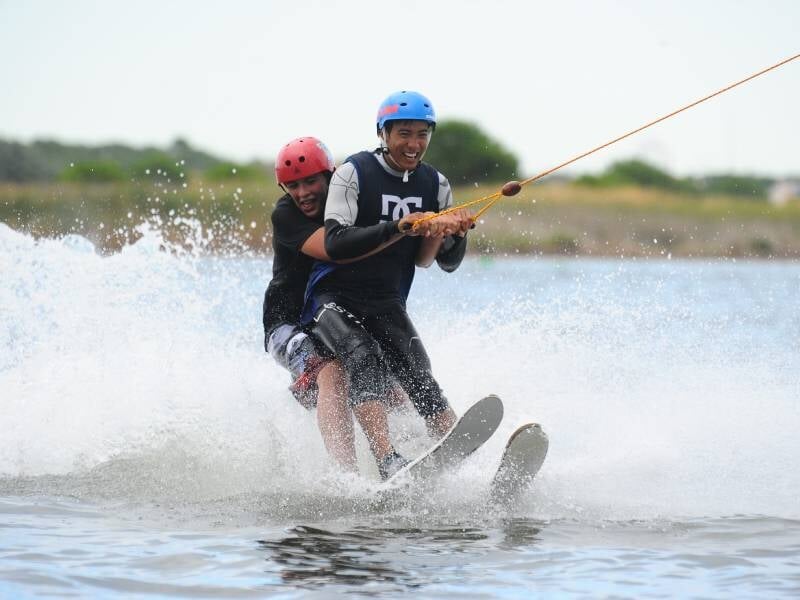 Duo de jeunes hommes en train de faire du ski nautique, tirés par un câble