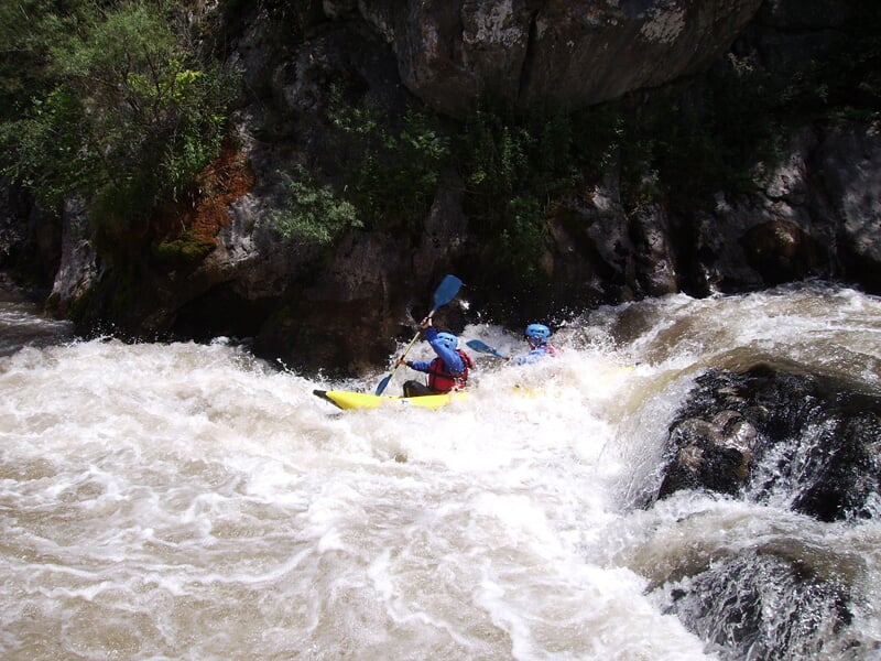 Deux personnes en kayak jaune naviguent dans des rapides tumultueux entourés de rochers et de végétation dense.