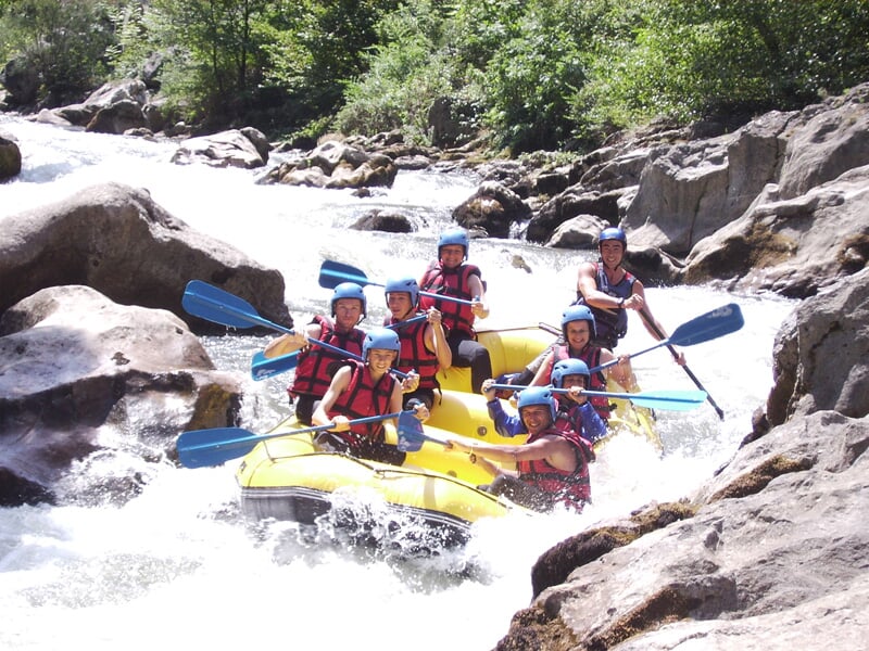 Groupe de six personnes en rafting sur un bateau jaune pagayant ensemble dans une rivière rocheuse et agitée.