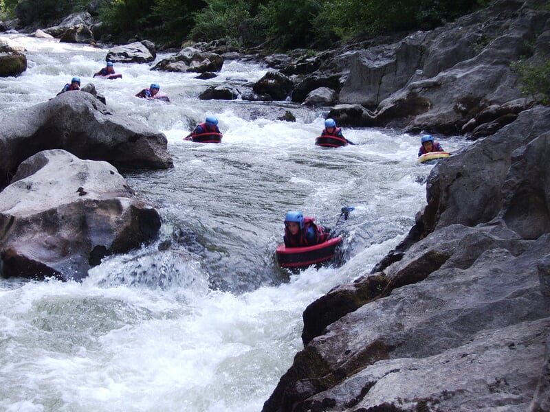 Plusieurs personnes en hydrospeed descendent une rivière rapide entre des rochers, équipées de casques et combinaisons.