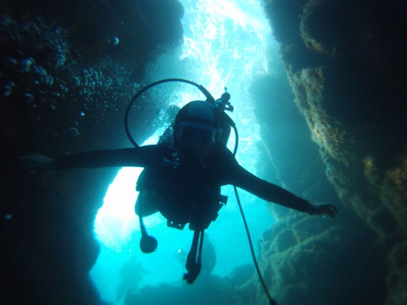 Plongeur explorant une grotte sous-marine éclairée par la lumière naturelle venant de l'entrée.