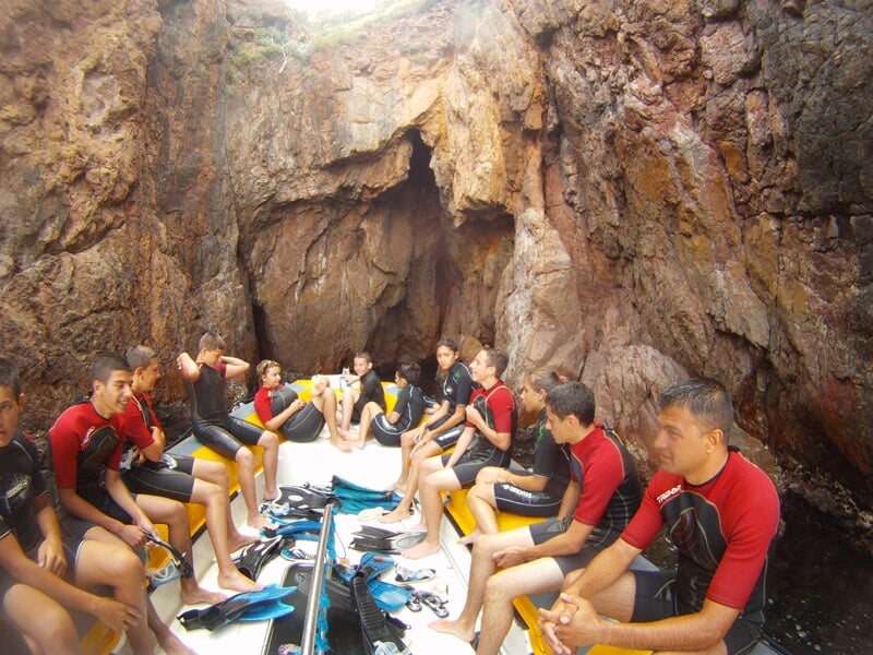 Groupe de plongeurs assis dans une grotte rocheuse, équipés de combinaisons et palmes.