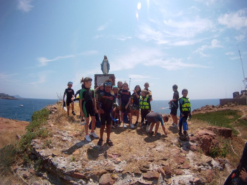 Groupe d'enfants en combinaison de plongée sur une île rocheuse, prêts pour une activité marine.