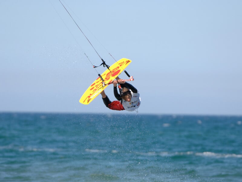 Kitesurfeur en plein saut avec une planche jaune au-dessus de la mer calme sous un ciel clair.