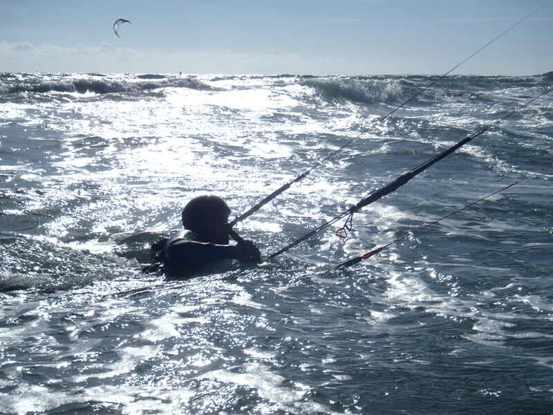 Kitesurfeur dans l'eau avec son aile, sous un ciel lumineux et une mer agitée par le vent.