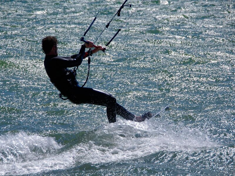 Kitesurfeur en combinaison noire glissant sur l'eau, tenant fermement la barre de contrôle.