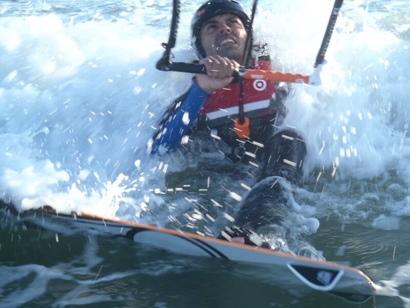 Kitesurfeur souriant sur sa planche, entouré d'éclaboussures d'eau en mouvement.