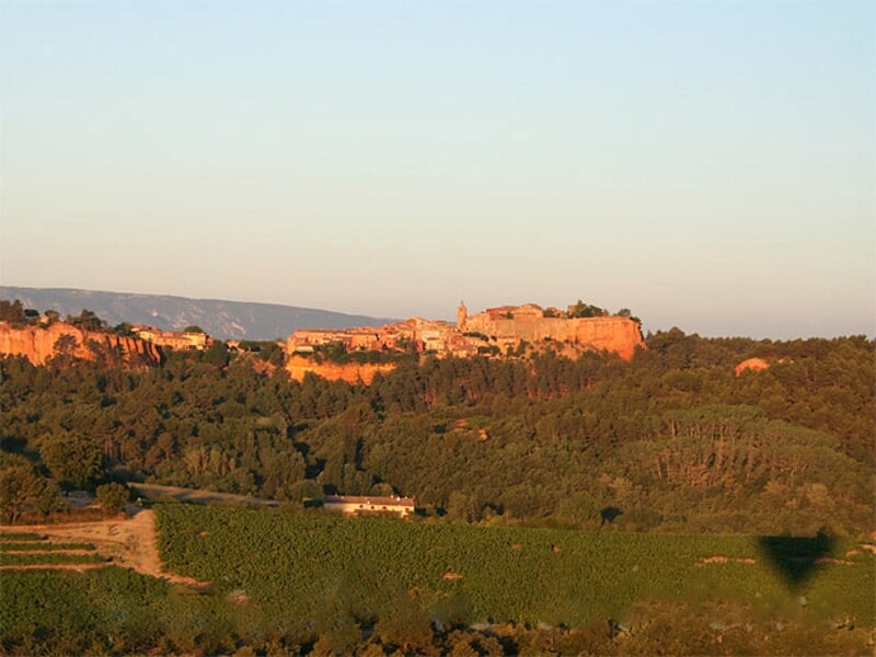 Montgolfière rouge en vol au-dessus d'un paysage vallonné avec un château en arrière-plan.
