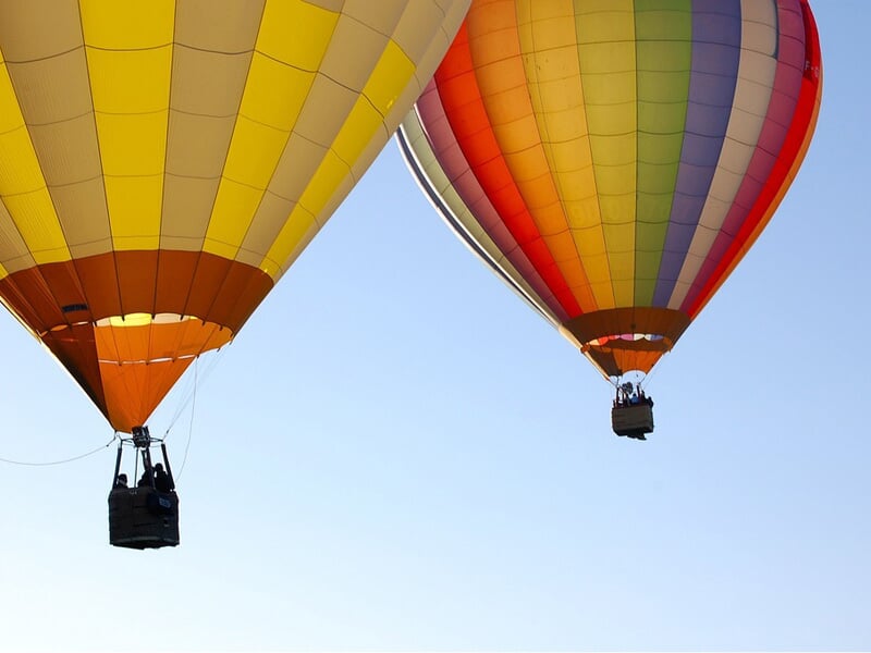 Deux montgolfières colorées flottant dans un ciel clair au-dessus d'un paysage naturel paisible.