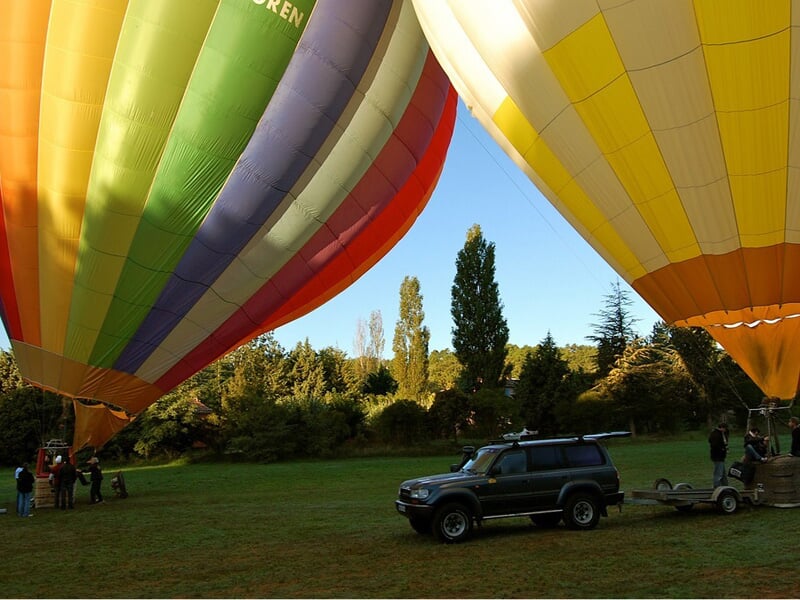 Montgolfières multicolores au sol dans un champ vert avec des personnes et un véhicule tout-terrain à proximité.