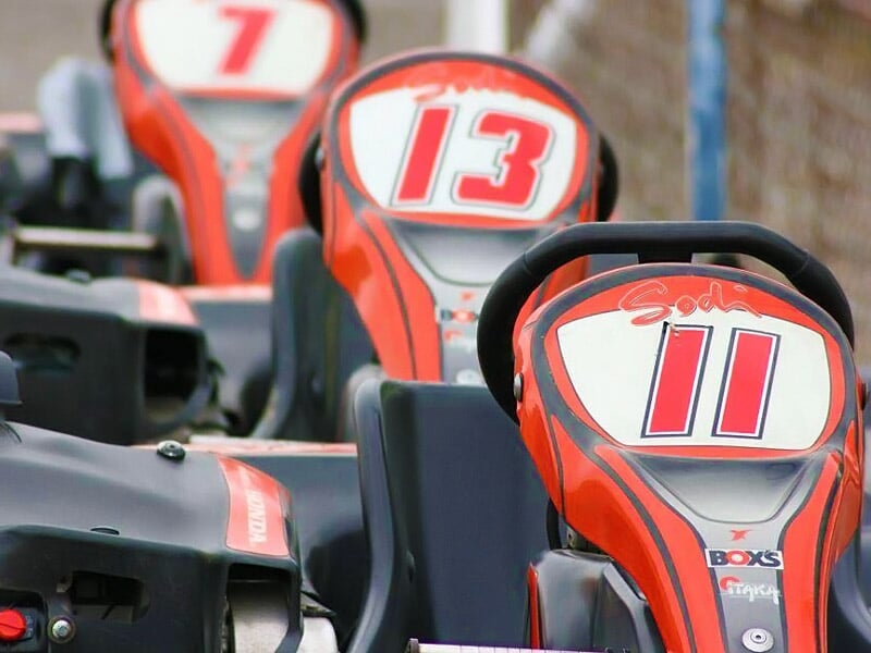 Gros plan sur trois karts rouges numérotés 7, 13 et 11 alignés en file sur une piste de karting.