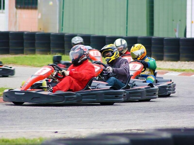 Quatre pilotes en karting en pleine course sur une piste, tous portant des casques et des combinaisons colorées.