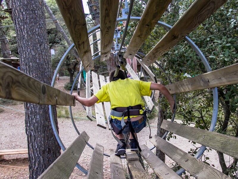Un enfant en tenue jaune avance dans un tunnel en bois suspendu dans un parcours d'accrobranche.
