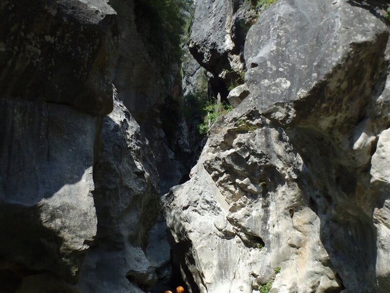 Canyon étroit avec de hautes parois rocheuses grises et végétation, idéal pour le canyoning en plein air.