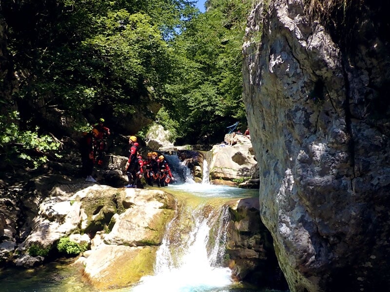 Groupe de personnes équipées de combinaisons et de casques, se préparant à descendre une petite cascade dans un canyon