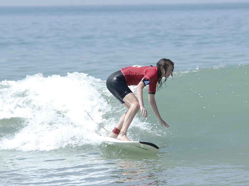 Jeune surfeuse en combinaison rouge et noire, debout sur sa planche blanche, glissant sur une vague calme à Longeville-sur-Mer.
