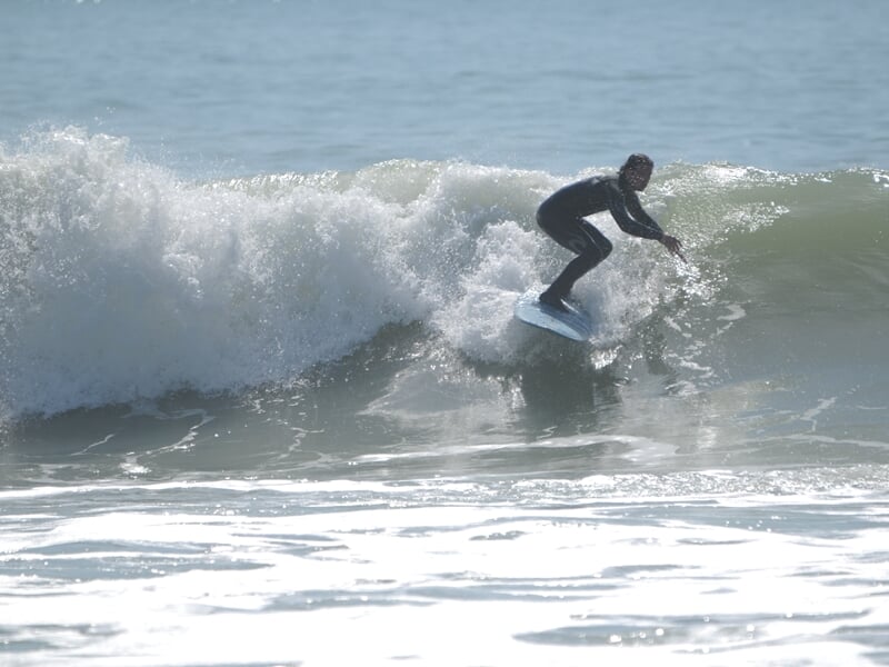 Surfeur en combinaison noire, debout sur sa planche blanche, surfant une vague plus grande avec concentration à Longeville-sur-Mer.