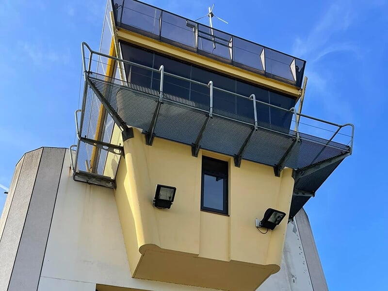 Tour de contrôle d'un aérodrome avec une structure jaune et des vitres panoramiques sous un ciel bleu