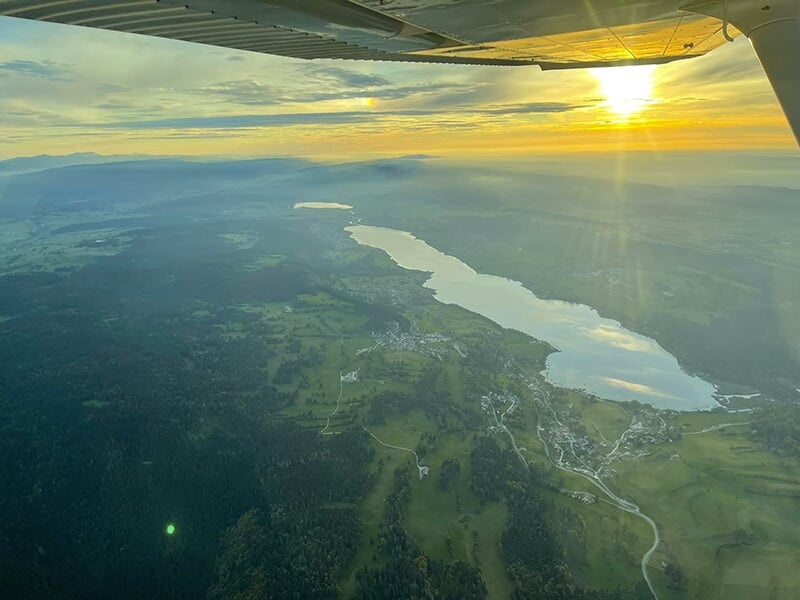 Vue aérienne d'un lac serpentant à travers une vallée verdoyante au coucher du soleil, prise depuis un avion.