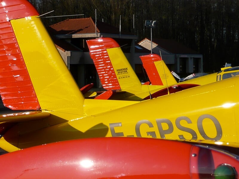 Rangée d'avions jaunes et rouges stationnés sur un aérodrome, avec leurs dérives marquées par des inscriptions.