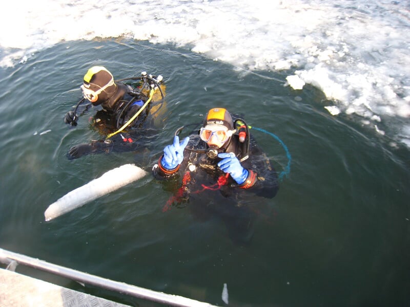 Deux plongeurs en combinaison noire sortant de l'eau glacée avec un signe de paix.