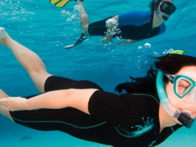 Deux personnes en masque et tuba nageant sous l'eau dans une mer claire et bleue.