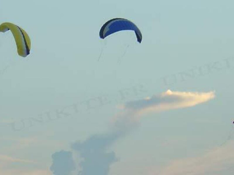 Deux kitesurfers avec leurs ailes colorées volent dans le ciel au-dessus de la mer au coucher du soleil.