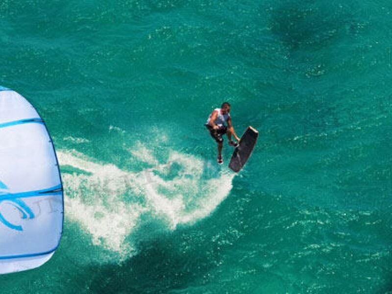 Vue aérienne d'un kitesurfeur glissant sur l'eau turquoise avec une aile bleue et blanche.