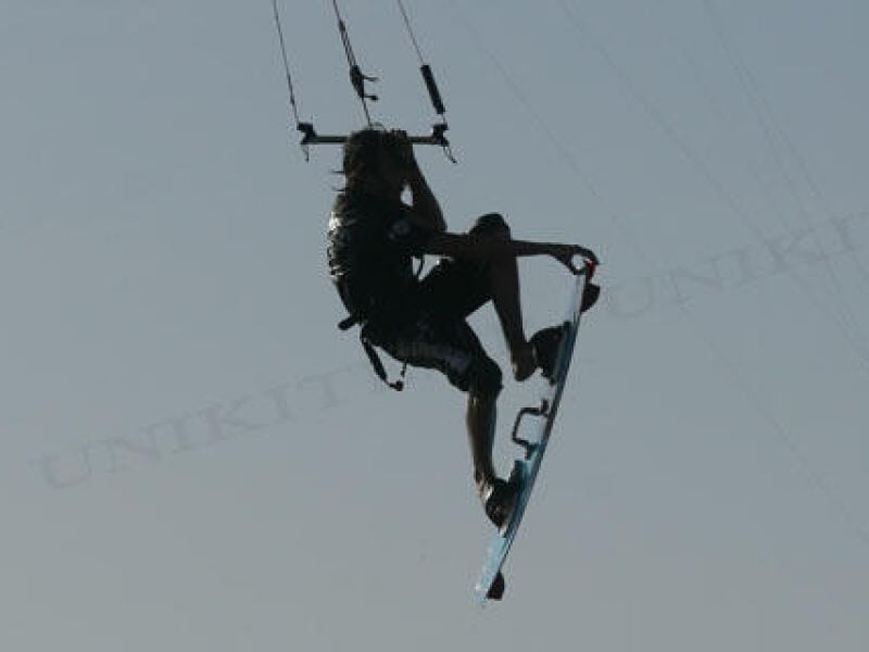 Kitesurfeur en plein saut avec sa planche, suspendu dans les airs avec son aile au-dessus.