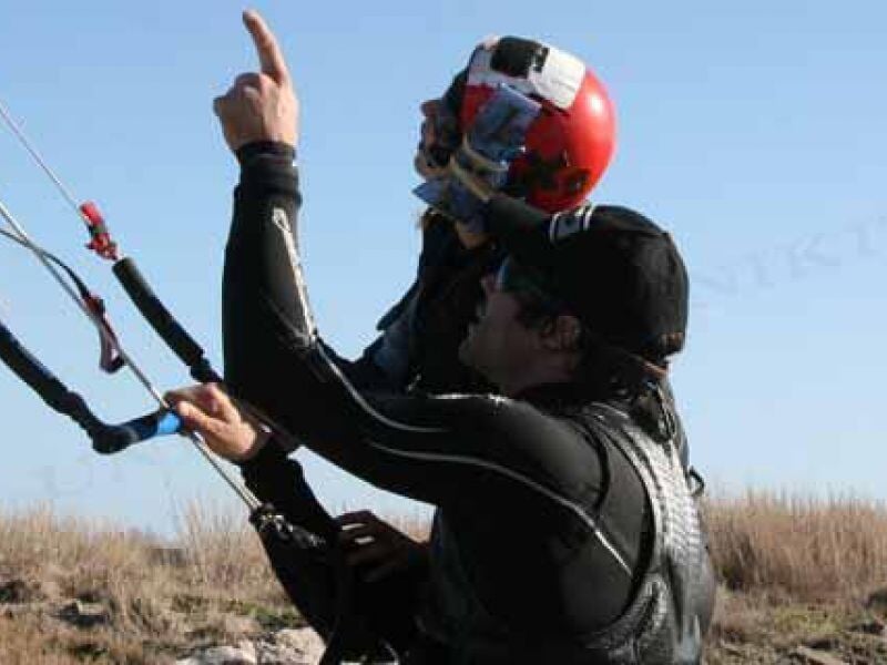 Instructeur en combinaison noire enseignant à un élève portant un casque rouge sur la plage.
