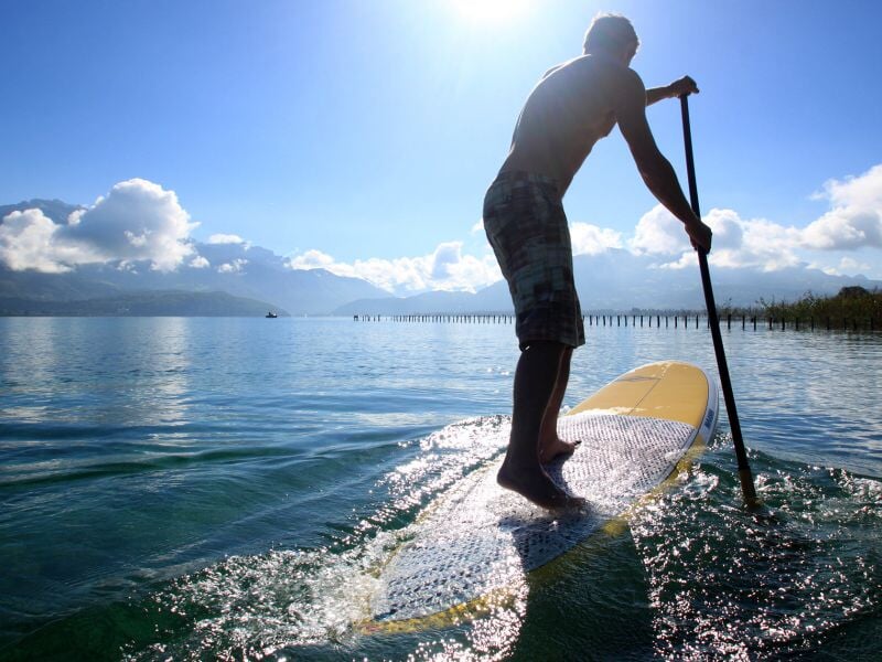Silhouette d'un homme pagayant sur un paddleboard au lever du soleil sur un lac paisible.