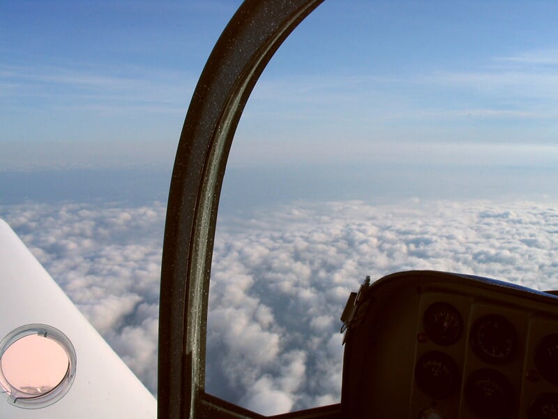 Intérieur d'un ULM avec vue sur un ciel bleu et un océan de nuages blancs en dessous.