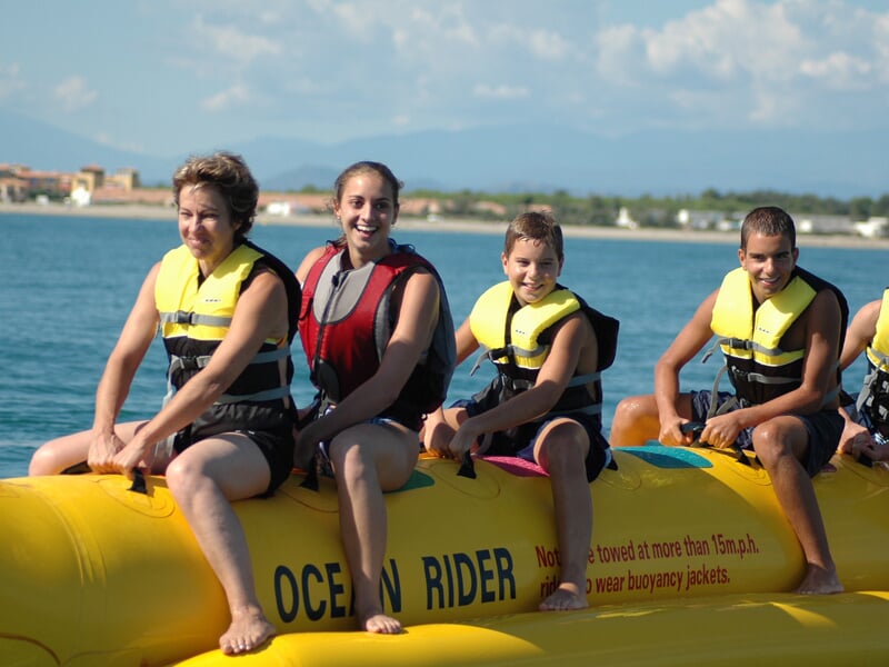 Quatre personnes souriantes portant des gilets de sauvetage jaunes et rouges assises sur un bateau gonflable jaune sur l'eau.