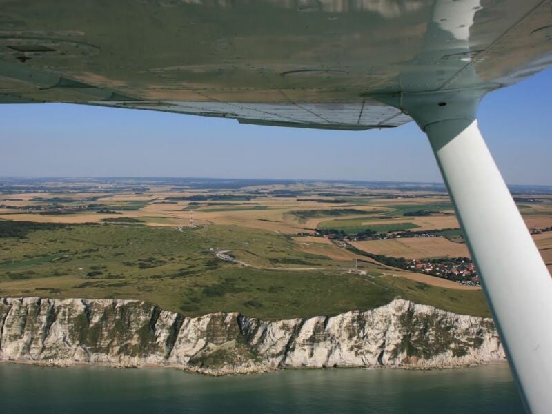 Vue aérienne depuis un avion montrant une côte rocheuse blanche et des champs verts sous un ciel dégagé.