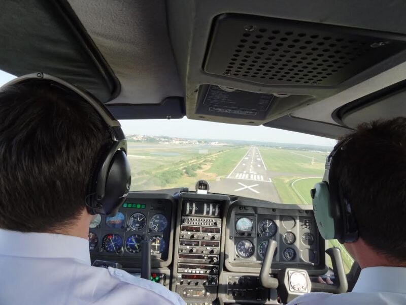 Cockpit d'un avion avec deux pilotes portant des casques, en approche d'une piste d'atterrissage visible.