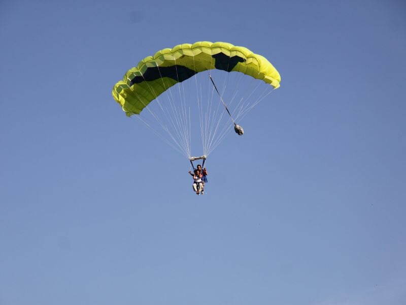 Parachutiste sous un parachute jaune et noir, descendant dans un ciel clair sans nuages visibles.