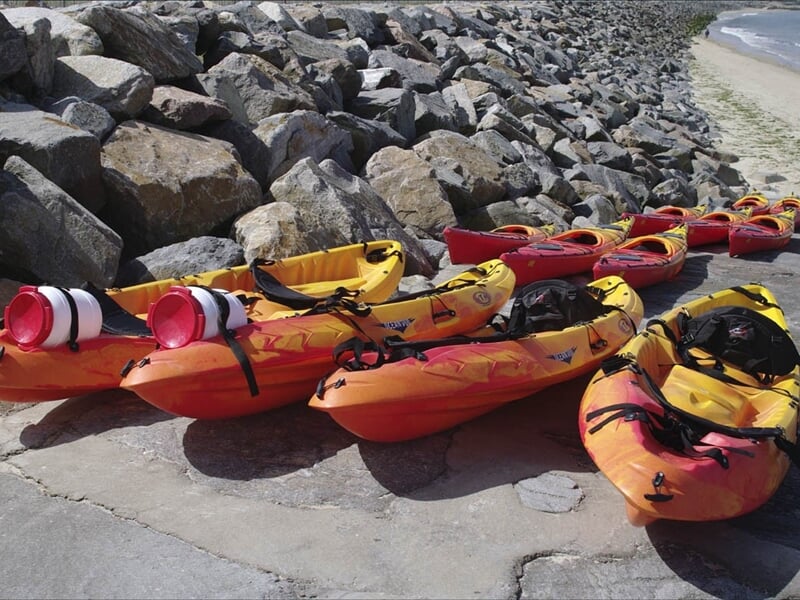 Plusieurs kayaks rouges et jaunes alignés sur un quai en béton près d'une plage rocheuse.