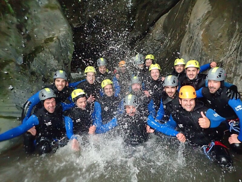 Groupe de personnes en combinaison et casque souriantes dans un bassin d'eau lors d'une activité de canyoning.