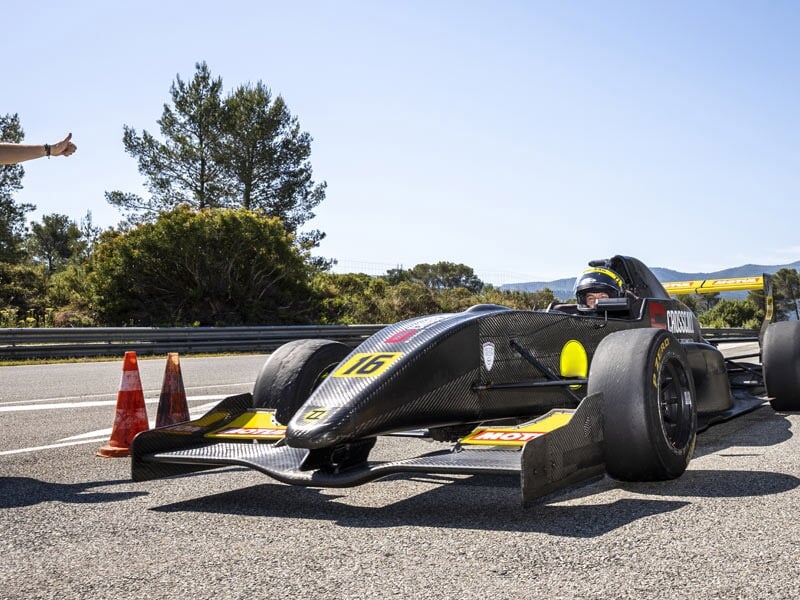 Formule Renault noire avec le numéro 16 garée sur la piste près de cônes orange et arbres.