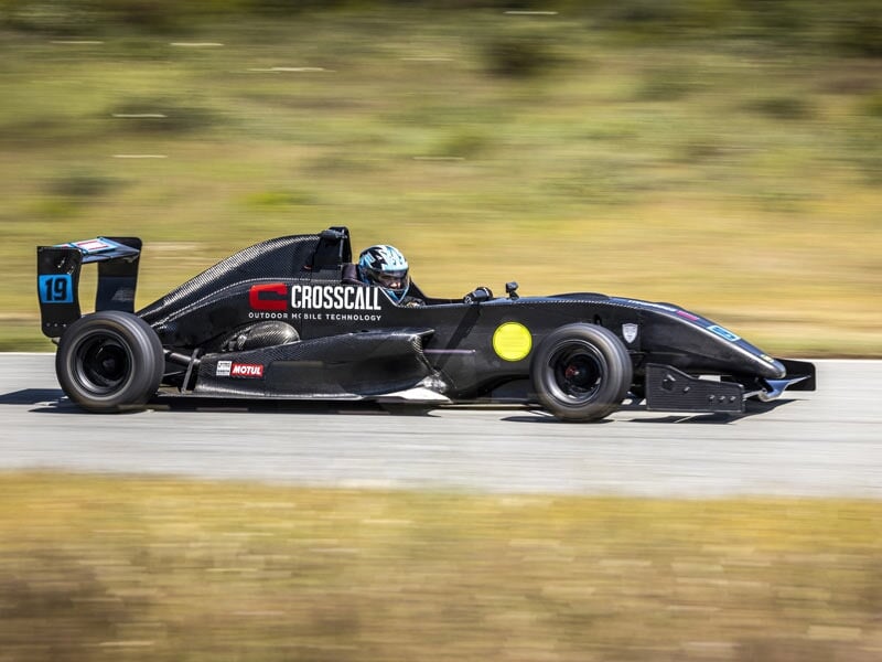 Formule Renault noire en course sur piste avec pilote casqué et décor flou de nature.